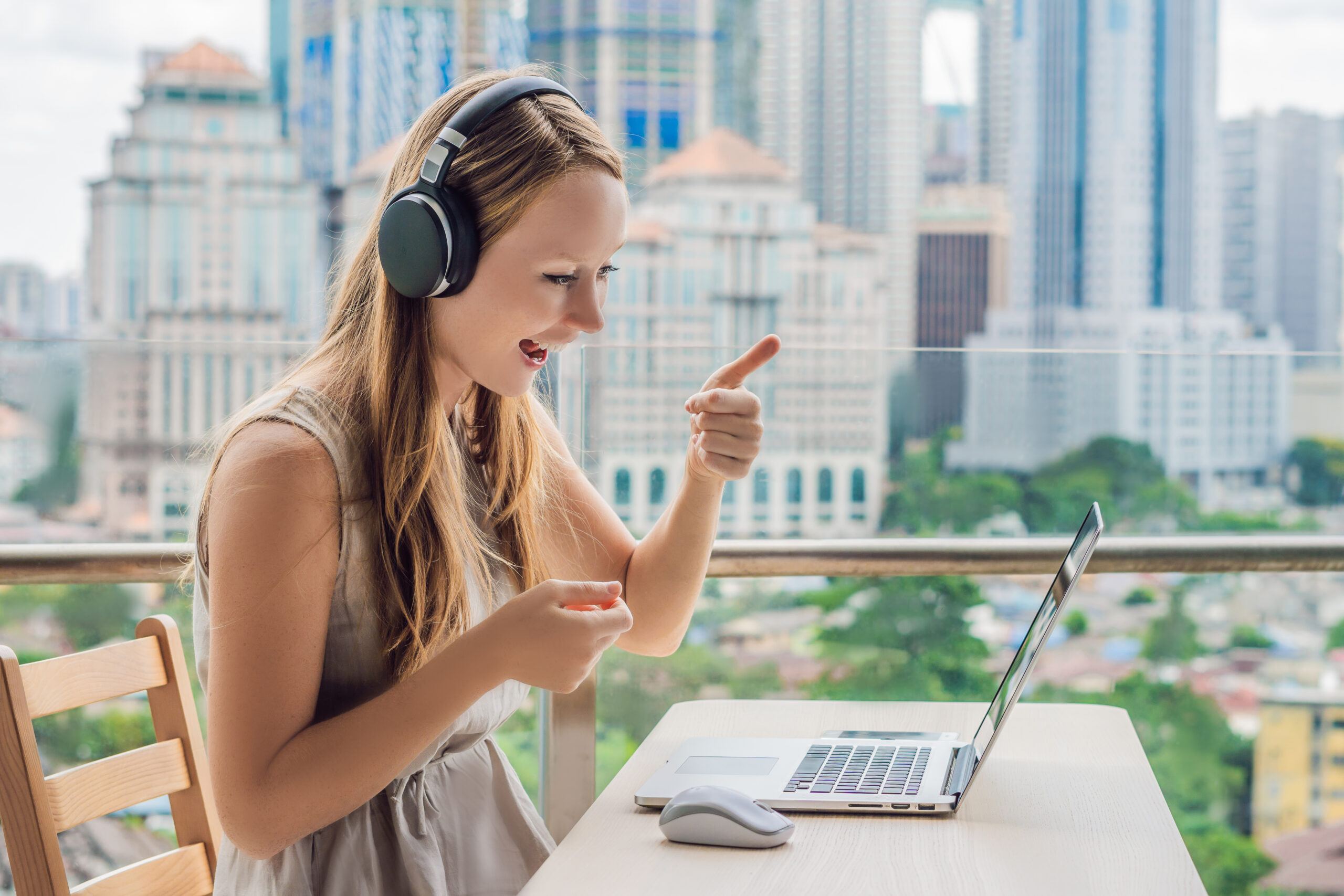 Young woman teaches a foreign language or learns a foreign language on the Internet on her balcony against the backdrop of a big city. Online language school lifestyle